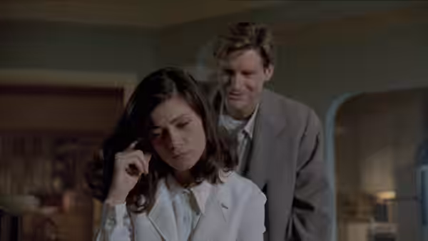 Bridget Gregory (Linda Fiorentino) presses a finger to her temple while a man stands behind her
