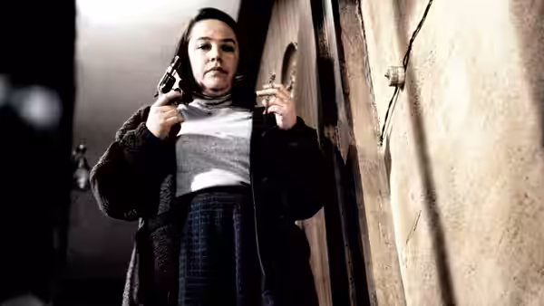 Annie Wilkes (Kathy Bates) holding a gun and cigarette indoors