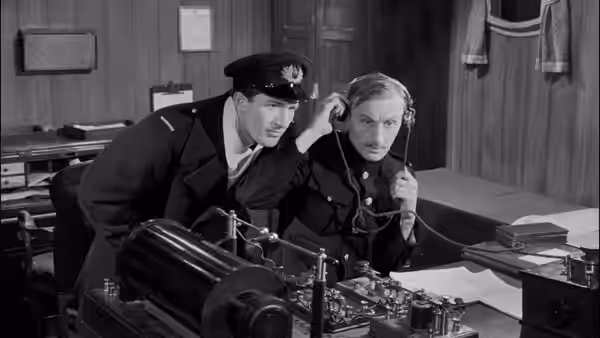 Two officers listen intently beside wireless equipment in a cabin