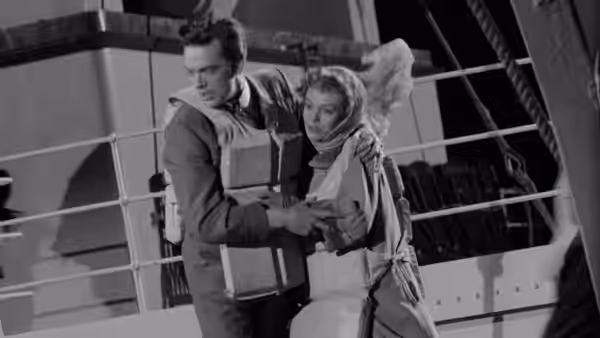 A man steadies a woman in a life jacket aboard ship
