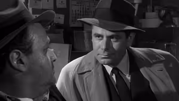 Dave Bannion, wearing a fedora and trench coat, talks to a man indoors
