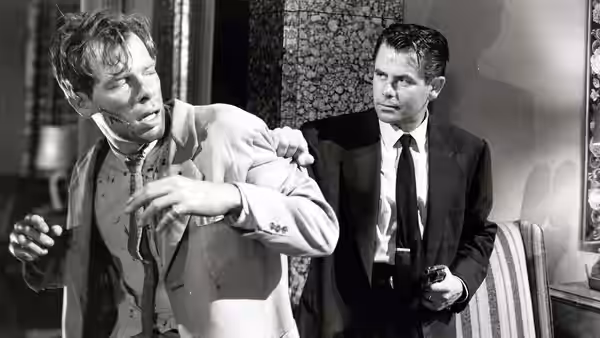 Dave Bannion restrains a man in a light suit inside a room