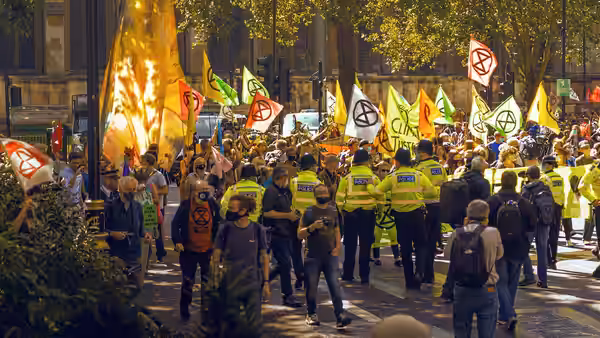 Police officers face a crowd of protesters carrying flags and banners along a city street