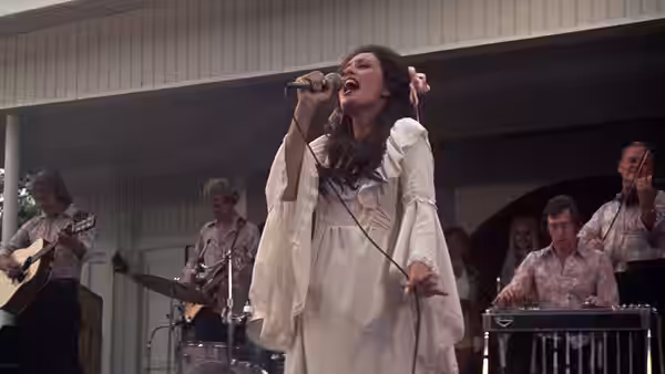 A woman in a white dress sings passionately on stage with her band behind her