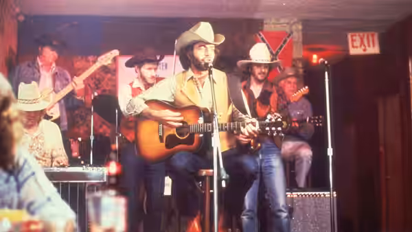 A man in a cowboy hat plays guitar and sings on stage with his band