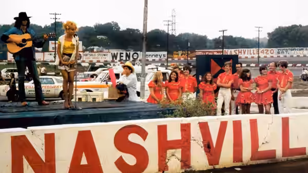 Singers perform on an outdoor stage in front of a large red Nashville sign