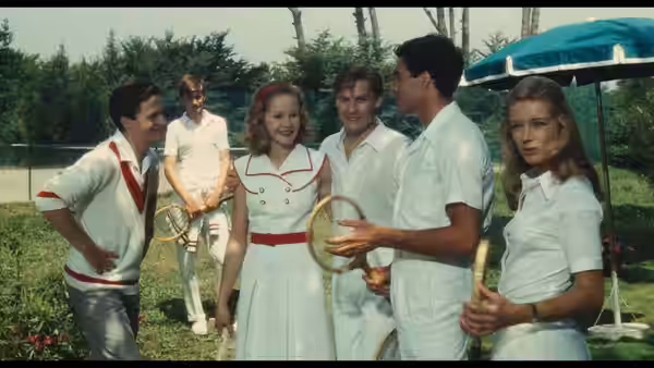 Young guests gather with tennis rackets beneath a garden umbrella