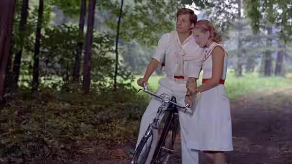 A young couple pause with a bicycle beside the garden’s glass doors