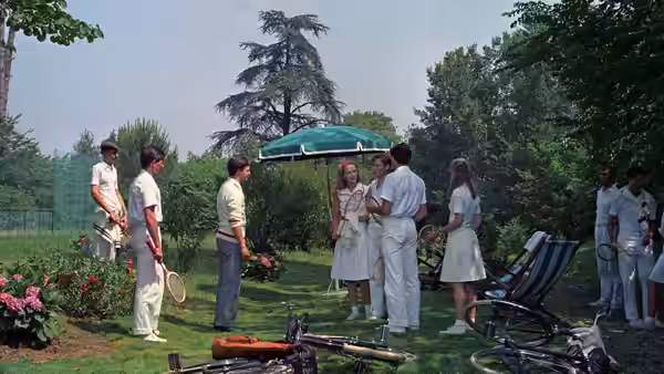 Guests mingle on the lawn beside tennis chairs and rackets
