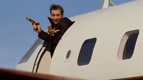 Nicolas Cage leaning from a white airplane holding a gun and golden mask