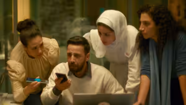 Four people examine phone and laptop screen in office