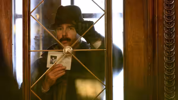 Inspector Stoppard (Sam Rockwell) holds up a document behind a glass door