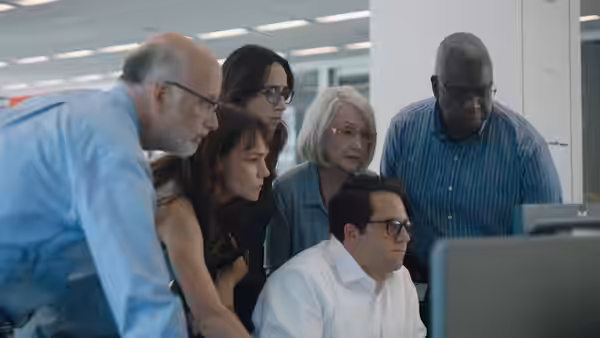 Newsroom colleagues gather around a computer, studying its screen together