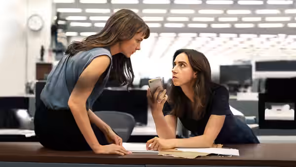 Megan Twohey (Carey Mulligan) leans over a desk to speak with Jodi Kantor (Zoe Kazan)