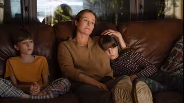 A woman sits on a couch with two boys, resting her hand on one child’s head