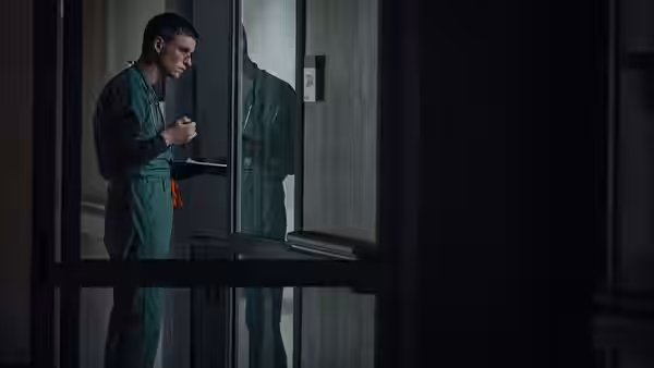 Charles Cullen (Eddie Redmayne) stands alone behind a glass door in hospital scrubs