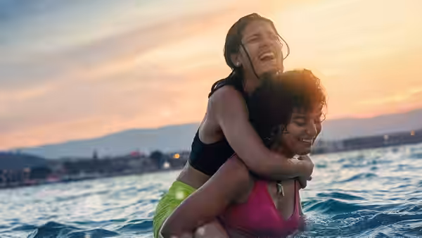Two young women in swimwear embrace in the sea at sunset