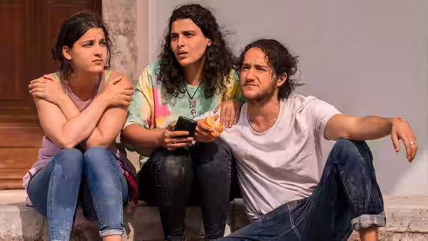 Two young women and a young man sit together outside a doorway