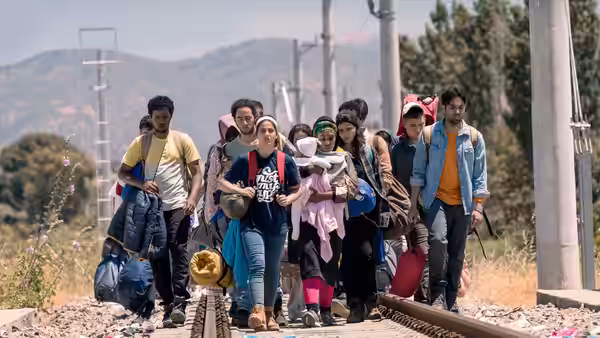 A group of migrants carrying bags walks along railway tracks through the countryside