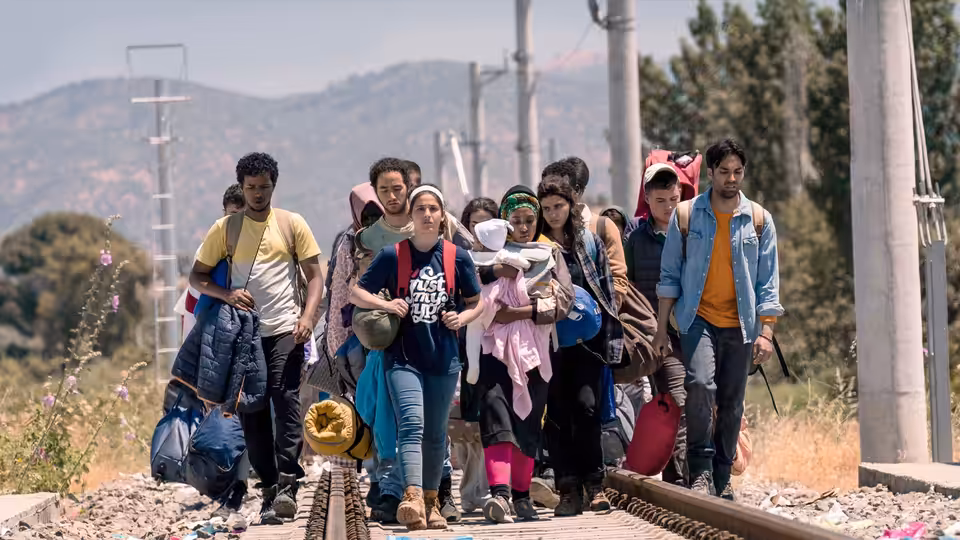 A group of migrants carrying bags walks along railway tracks through the countryside