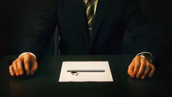 A suited man rests his hands beside a pencil and bloodied exam paper