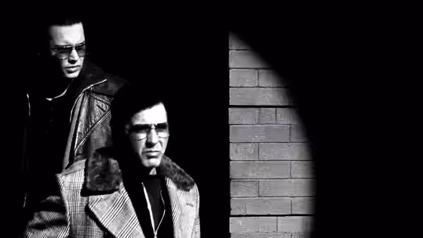 Lefty (Al Pacino) standing in front of another man near a brick wall