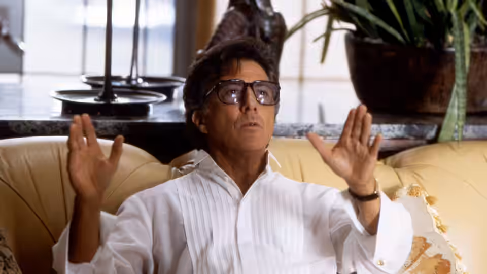Stanley Motss (Dustin Hoffman) raises both hands while seated on a couch