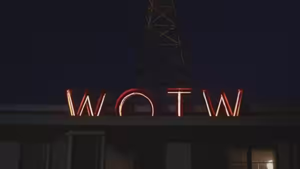 The illuminated WOTW radio station sign sits below a transmission tower at night