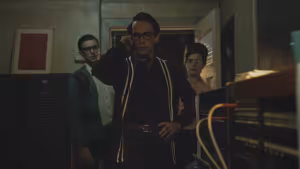 Everett (Jake Horowitz) holds a telephone as two men stand behind him in the station