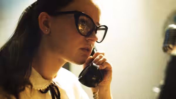 Fay Crocker (Sierra McCormick) listens on a telephone beside a studio microphone