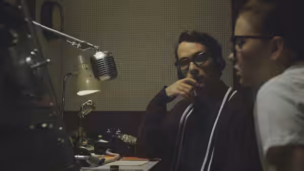 Everett (Jake Horowitz) speaks with a colleague beside a microphone in the radio booth
