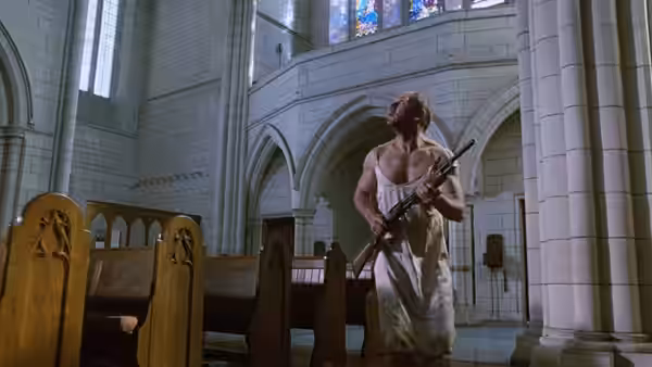 A man with a rifle stands inside a large empty church looking upwards