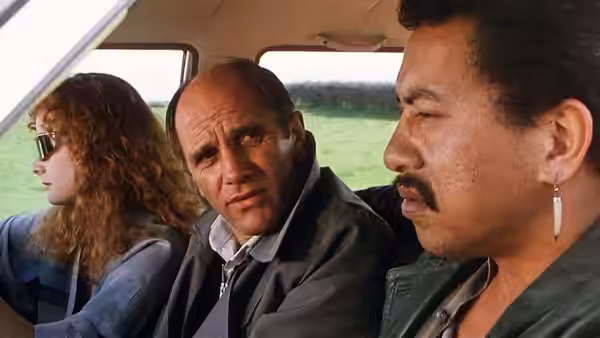Zac Hobson (Bruno Lawrence) sits between two companions inside a vehicle