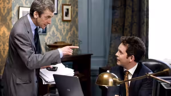 Malcolm Tucker (Peter Capaldi) pointing at seated Toby Wright (Chris Addison) in an office