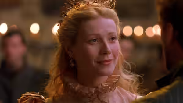 Viola De Lesseps (Gwyneth Paltrow) smiling warmly in a golden gown and crown