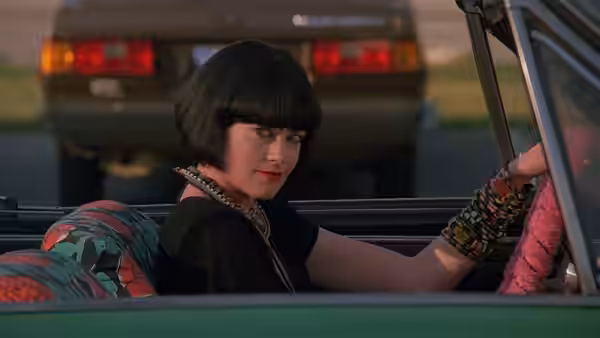 Audrey Hankel drives a green convertible at night with another car behind