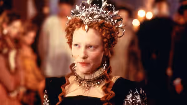 Elizabeth (Cate Blanchett) wearing a crown and jeweled necklace in formal attire