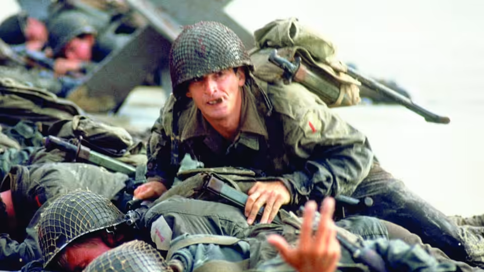 Griff (Mark Hamill) crawls over fallen soldiers with a rifle slung across his back
