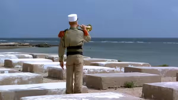 A Legionnaire plays a bugle among concrete blocks beside the sea