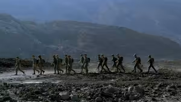 French Foreign Legionnaires march across a rocky landscape beneath distant mountains