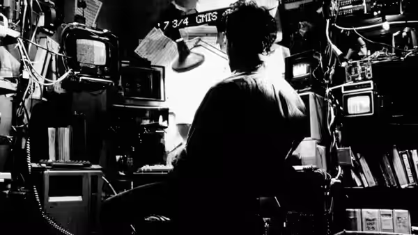 Maximillian Cohen works at computers in a cluttered apartment workspace