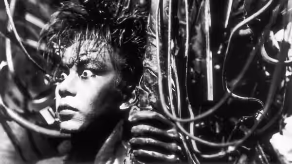 Salaryman (Tomorowo Taguchi) entangled in metal wires staring with wide eyes