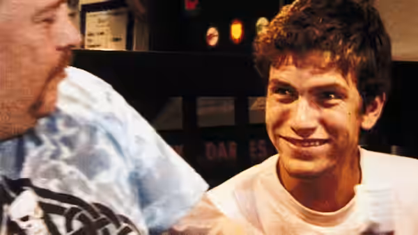 Two men sitting at a bar one smiling while looking at the other