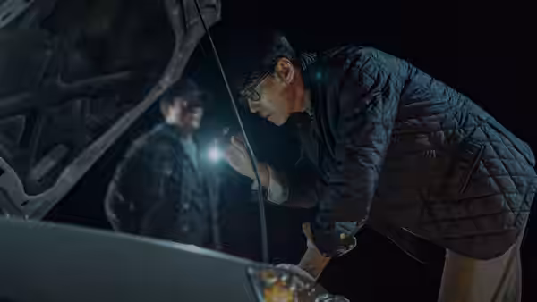 a man with glasses inspecting a car engine with a flashlight at night
