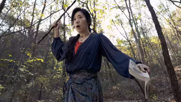 a woman holding a stick and an open book in a forest