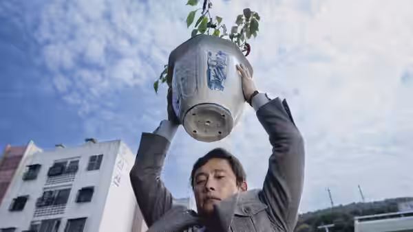 Man-su (Lee Byung-hun) lifting a large potted plant overhead outdoors