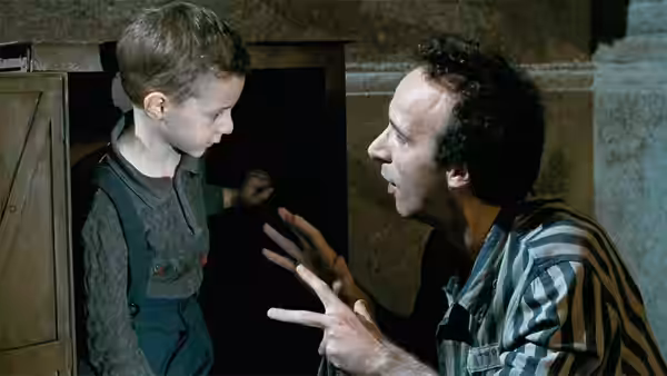 Guido (Roberto Benigni) gesturing to Giosué (Giorgio Cantarini) in a dark doorway