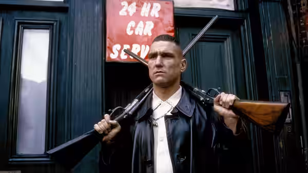A man in a leather jacket carries two shotguns on his shoulders