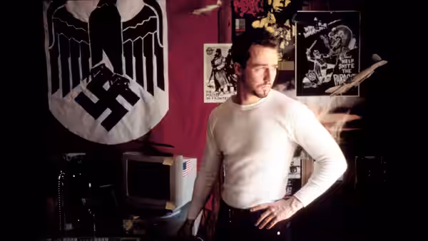 Derek (Edward Norton) standing with hand on hip before a flag