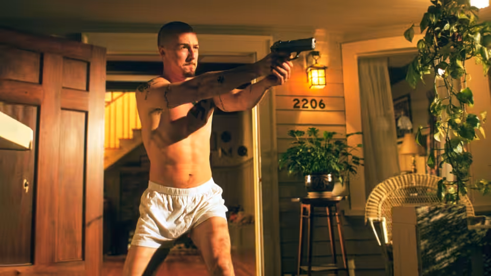 Derek (Edward Norton) aiming a handgun while standing in a house